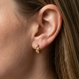 Close up on ear of 18ct gold plated chunky wave huggie hoop earrings